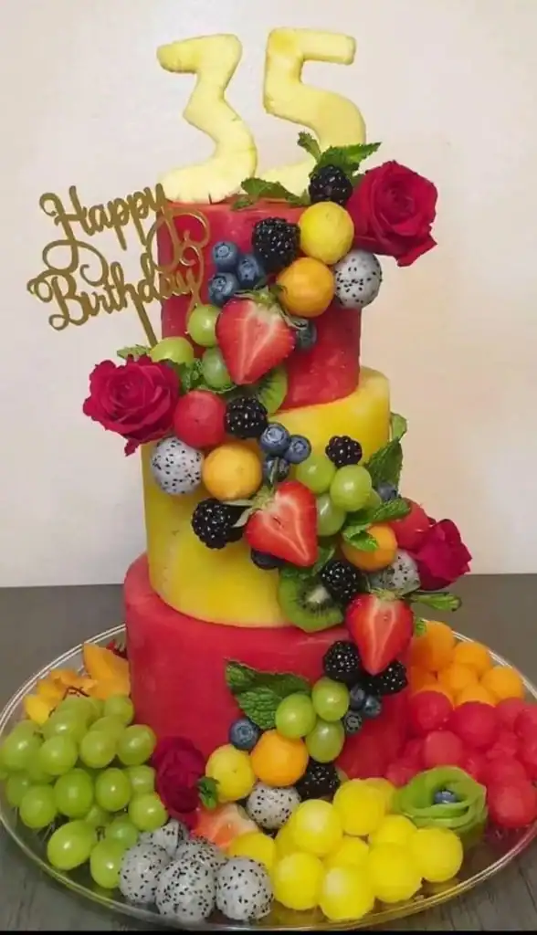Fresh fruit birthday cake topped with strawberries, blueberries, grapes, and roses arranged in concentric patterns