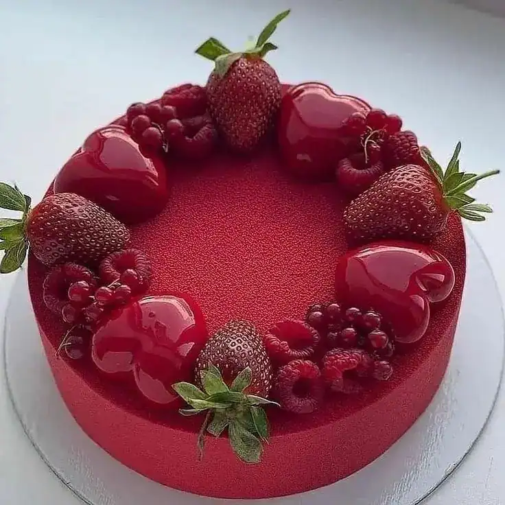 Red velvet cheesecake cake with cream cheese frosting and fresh red berries showing the layered interior