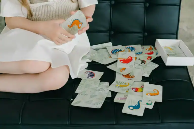 Kids playing memory matching game with dinosaur cards on black sofa.
