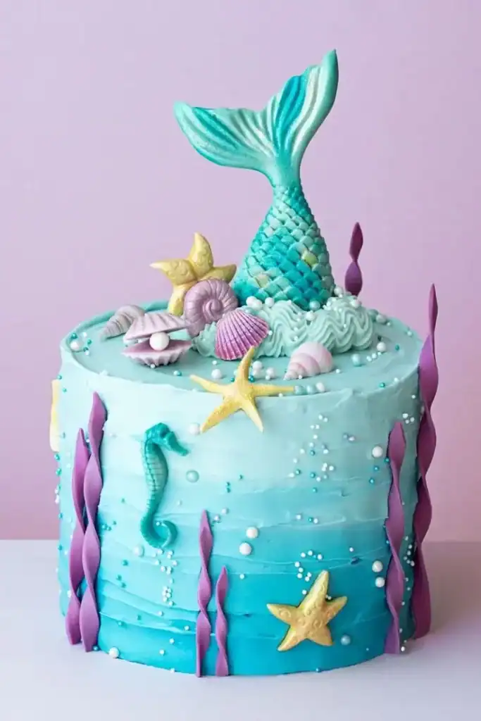 Mermaid-themed birthday cake with sculpted tail, ocean-blue buttercream, edible pearls, and shimmer decorations