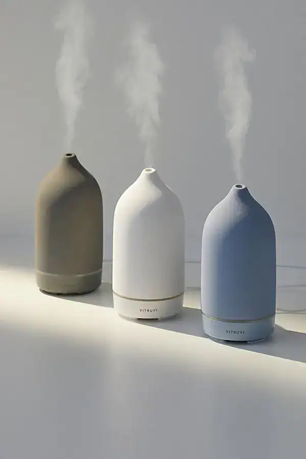 Essential oil diffusers in beige, white, and blue emitting gentle mist.