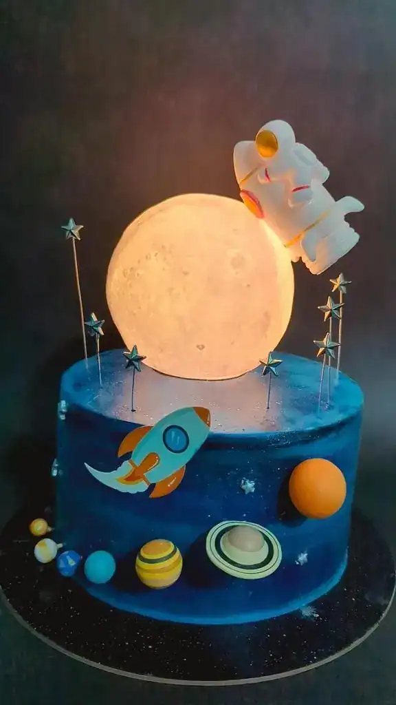 Space-themed birthday cake with black buttercream galaxy background, edible star glitter, fondant planets, and rocket decorations