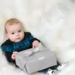 17 Winter Birthday Outfit Ideas Baby holding a gift box in a cozy winter setting for a birthday celebration.
