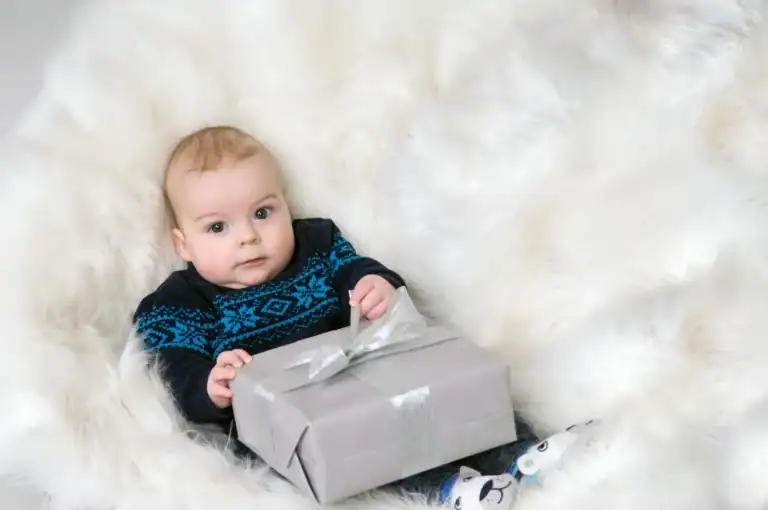 Baby holding a gift box in a cozy winter setting for a birthday celebration.