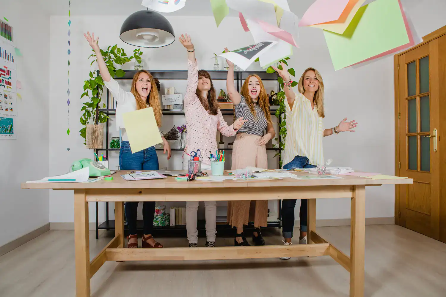 Women celebrating Spirit Week at work with papers flying in an office setting.
