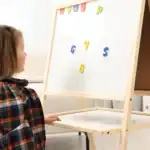 19 Engaging Whiteboard Games for All Ages Child playing with magnetic letters on whiteboard for engaging educational games.
