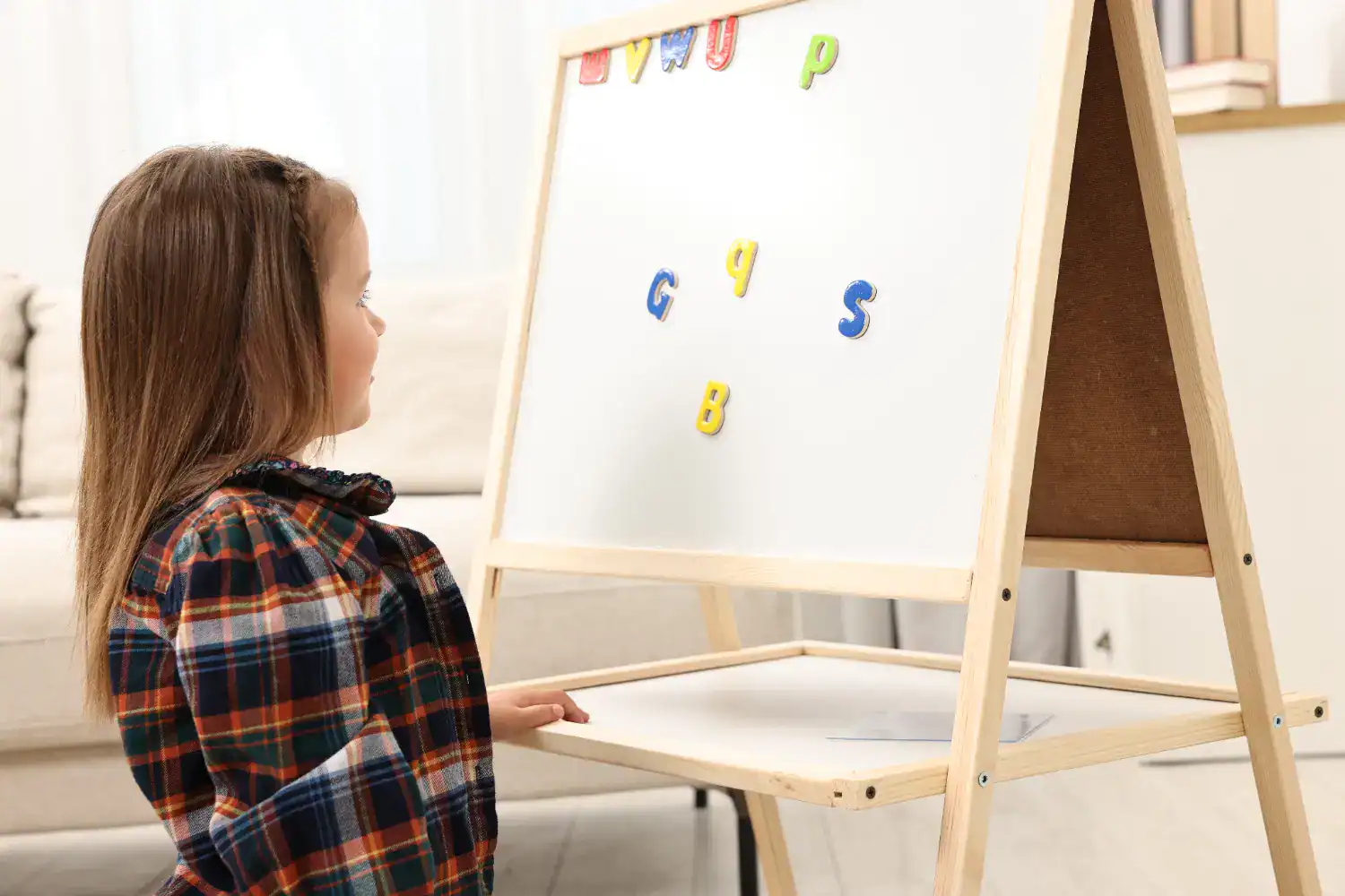 Child playing with magnetic letters on whiteboard for engaging educational games.