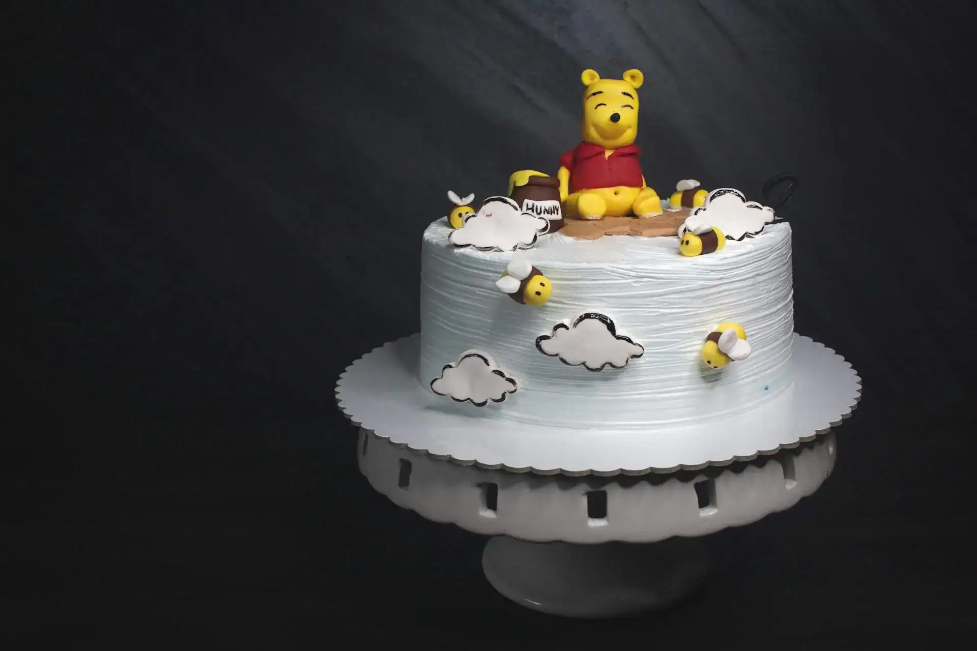 Winnie the Pooh themed birthday cake with clouds and bees for kids' celebration.