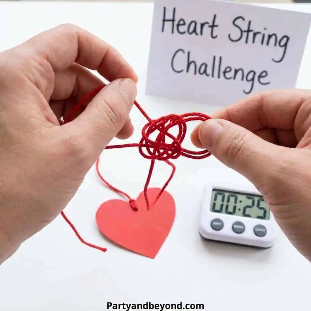 Hands tying a red string around a paper heart for Valentine's Day game activity.