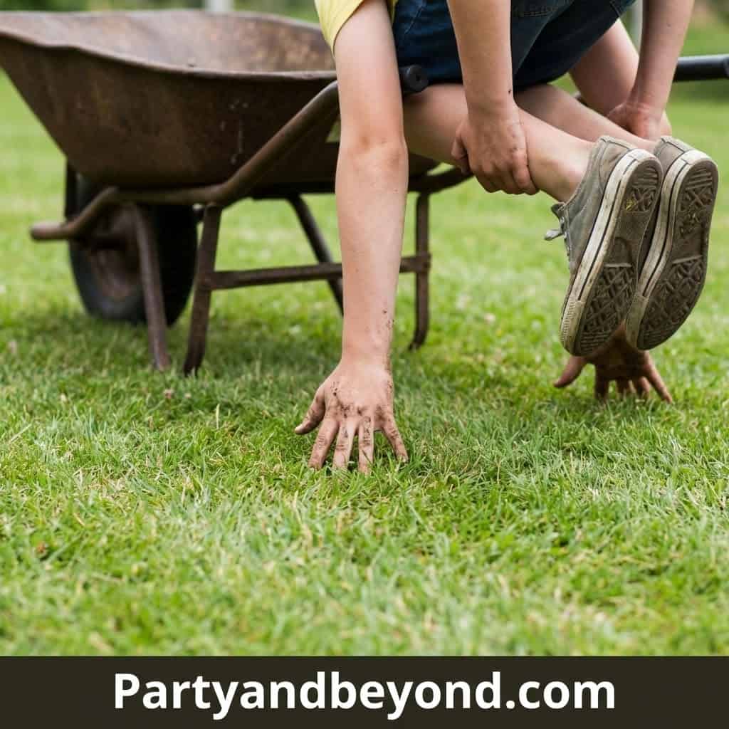 Child participating in outdoor field day game, crawling on grass with wheelbarrow in background.