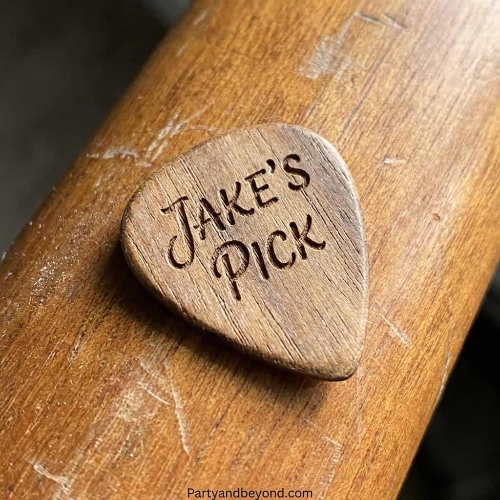 Personalized wooden guitar pick engraved with "Jake's Pick" on a wooden surface.