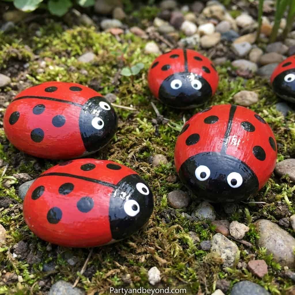Colorful ladybug rocks with googly eyes on mossy ground, perfect for kids' outdoor spring craft proj.