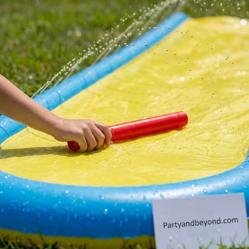 Child sliding on a yellow inflatable water slide with a red mat outdoors.