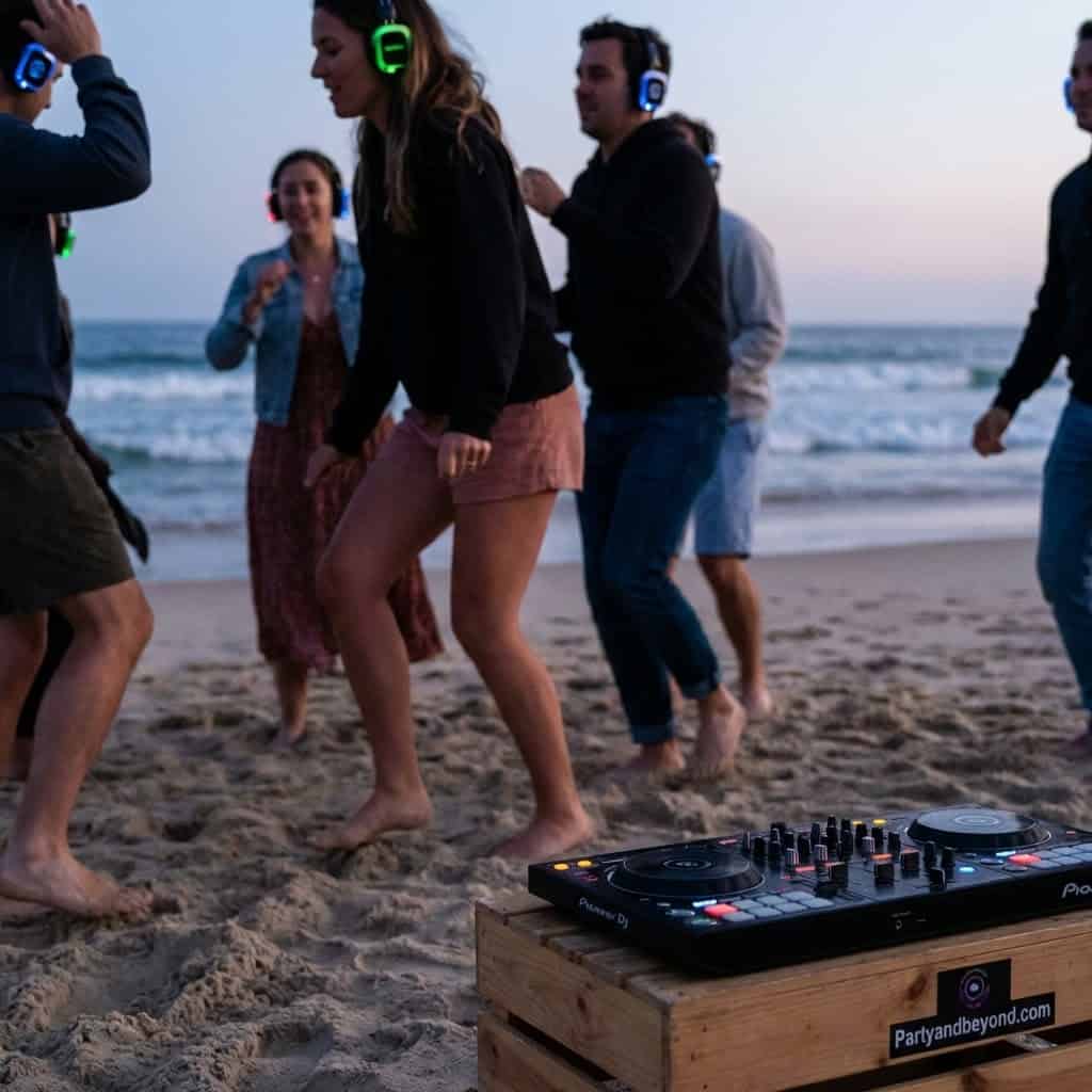 DJ playing music at a beach birthday party with friends dancing barefoot on the sand.