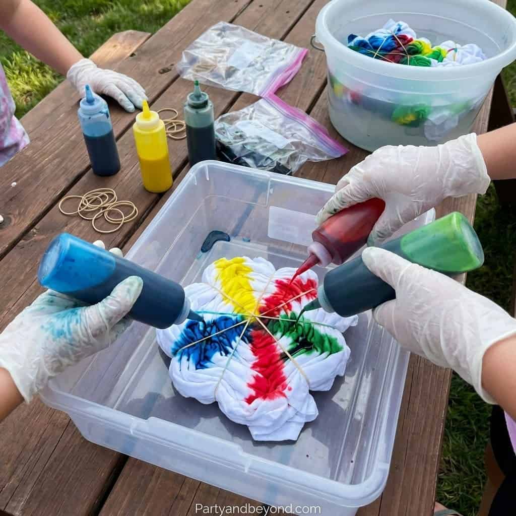 Kids creating vibrant tie-dye designs with squeeze bottles and rubber bands.