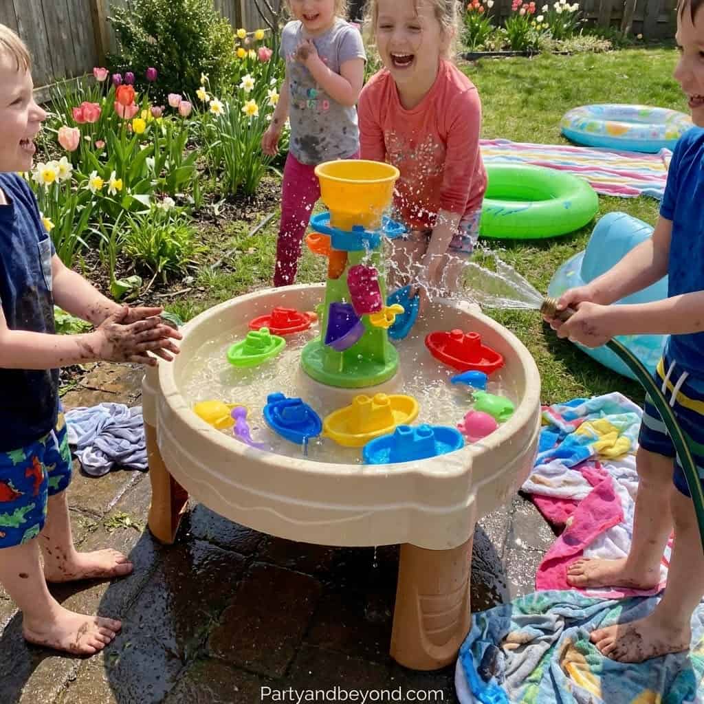 Outdoor kids' water table with colorful toys and splashing children.