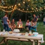 19 Low Budget Backyard Birthday Party Ideas for Adults Group of adults enjoying a backyard birthday party with string lights and a fire pit.