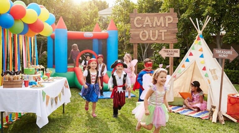 Kids enjoying a themed outdoor birthday party with a bounce house and camping setup.