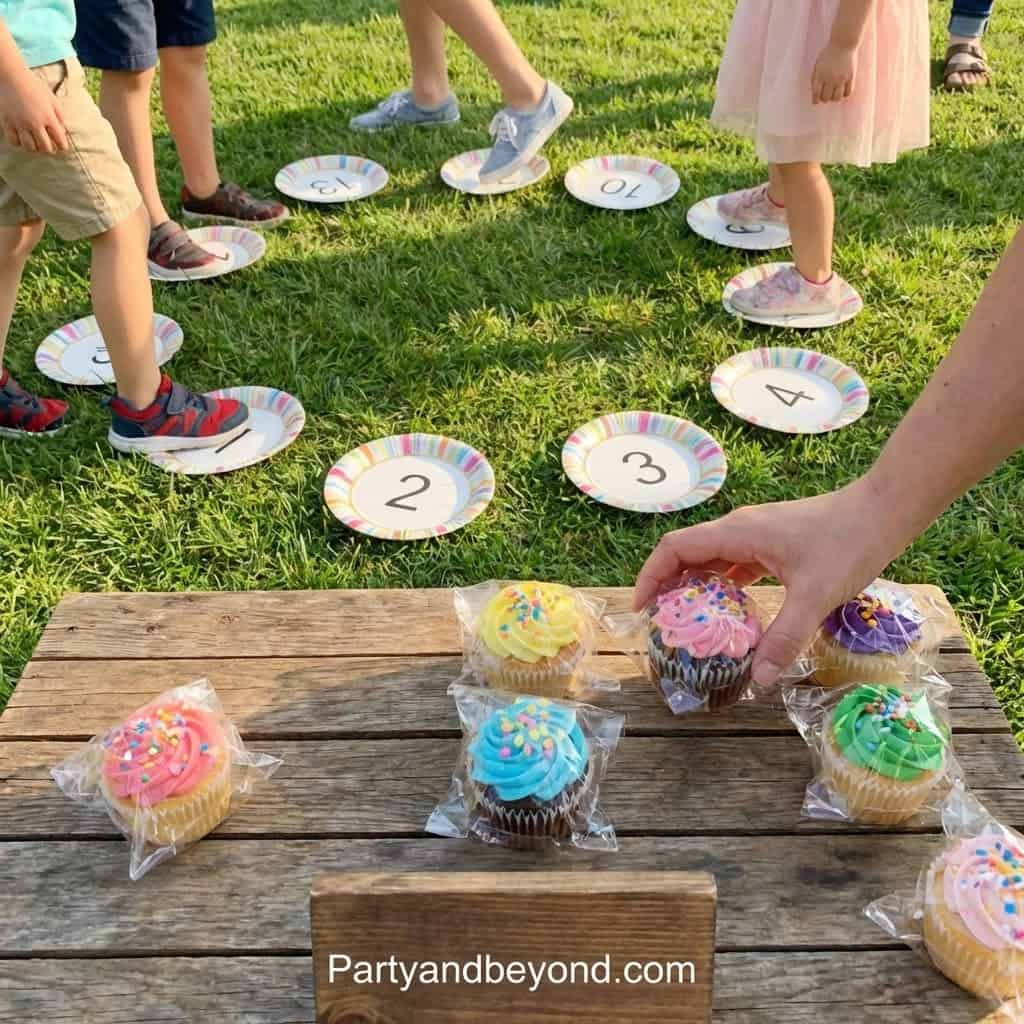 Kids playing outdoor hopscotch game with cupcakes at birthday party.
