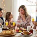 25 Best Mothers Day Brunch Ideas at Home That Will Make Her Cry Happy Tears (2026) Family enjoying Mother's Day brunch with flowers and breakfast foods at home.