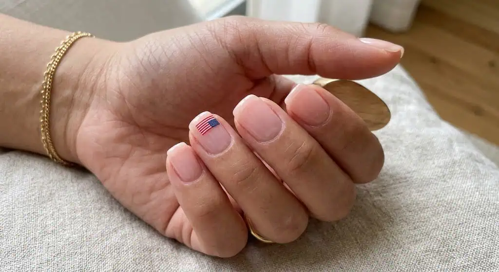 Minimal clear nail design featuring a tiny American flag accent with negative space styling.