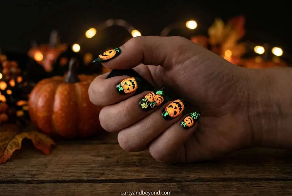 Glow-in-the-dark Halloween pumpkin nails shining in nighttime lighting. Pumpkin Nail Ideas