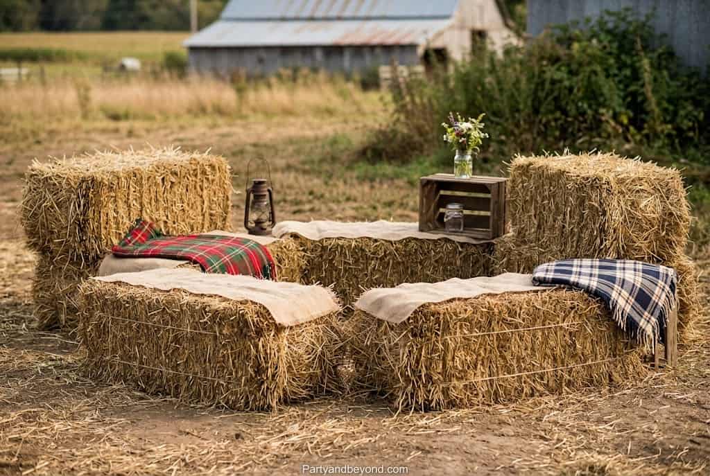 Rustic outdoor party seating made from stacked hay bales decorated with plaid blankets and cozy throw pillows.