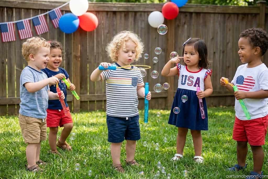 Children playing with bubbles at a festive outdoor birthday party with balloons and decorations.
