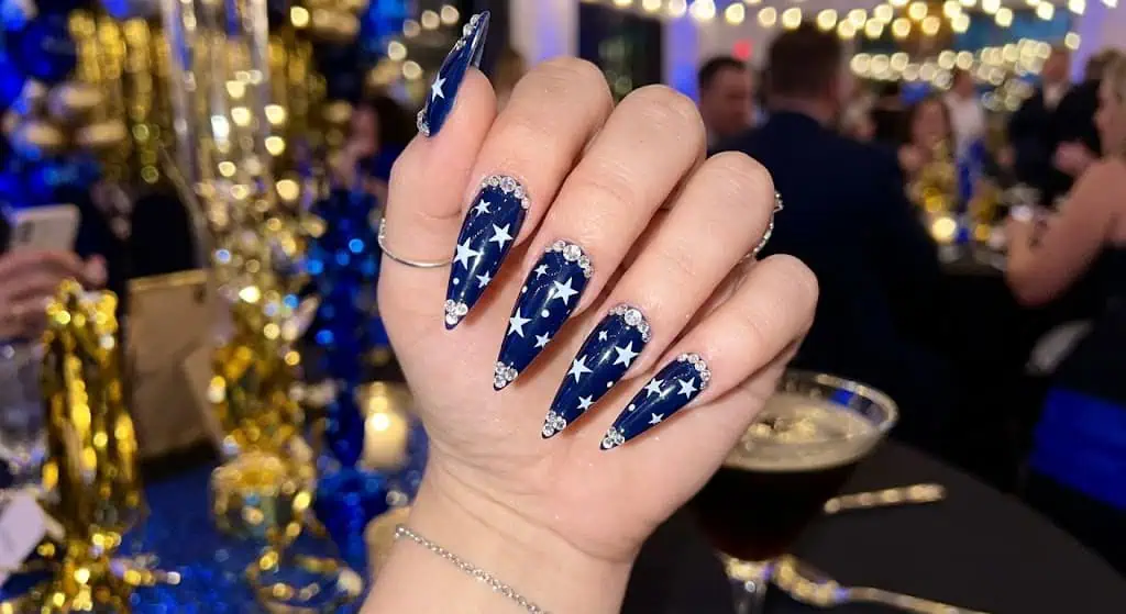 Stiletto-shaped navy nails with stars and rhinestones for dramatic patriotic manicure