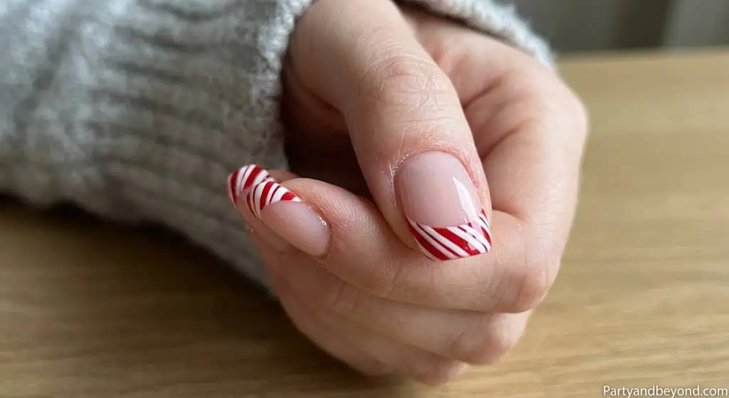 French tip nails with red diagonal stripes on white base for a candy-inspired patriotic style.