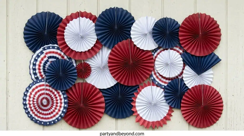 Colorful paper fan wall backdrop in red, white, and blue for a 4th of July photo corner.