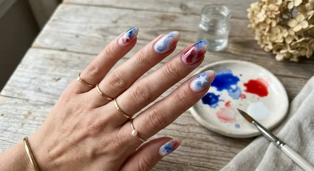 Soft watercolor-style nails blending red and blue on a sheer white base.