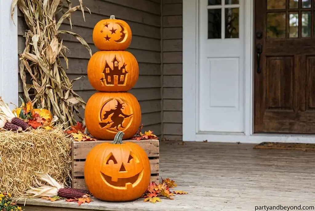 Three stacked carved pumpkins with funny Halloween expressions on porch steps.