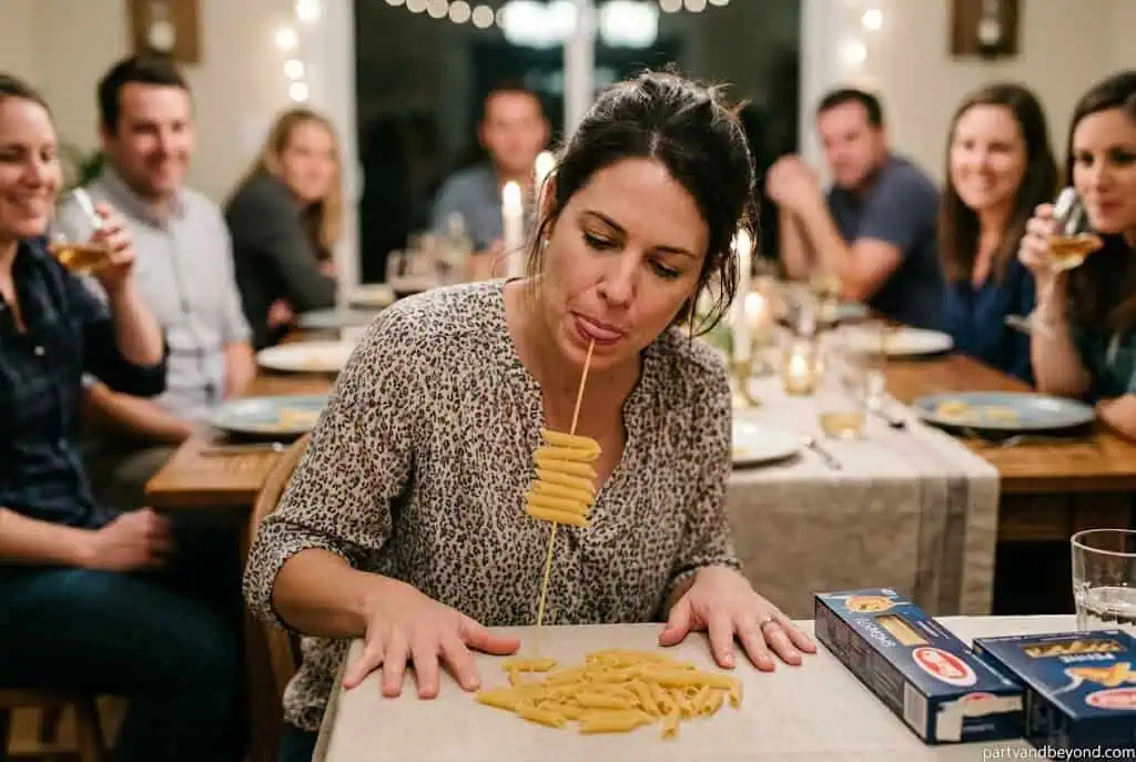Player threading penne pasta onto uncooked spaghetti held in their mouth during a minute to win it challenge