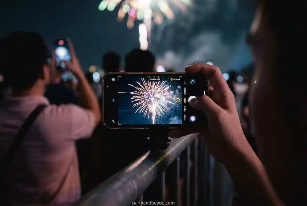 Person capturing fireworks on smartphone at night celebration.