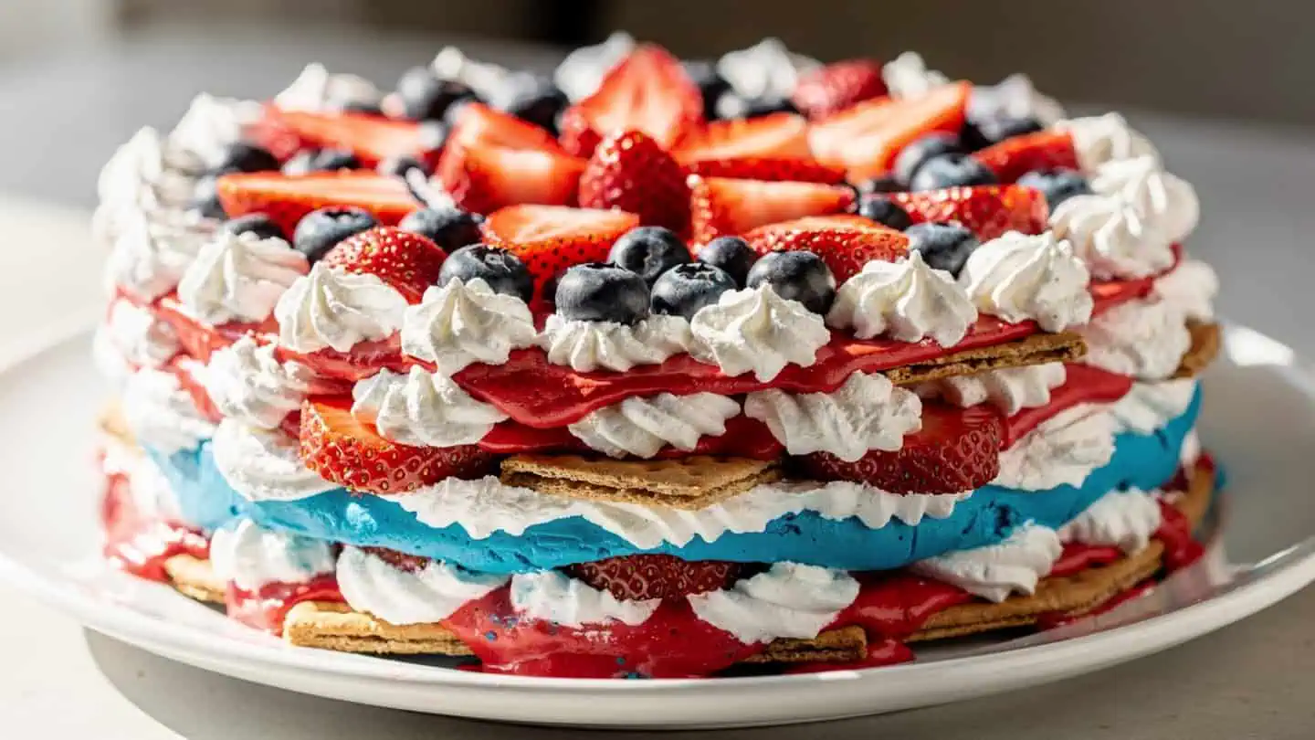 Slice of patriotic no-bake icebox cake showing layers of Cool Whip, graham crackers, strawberries, and blueberries