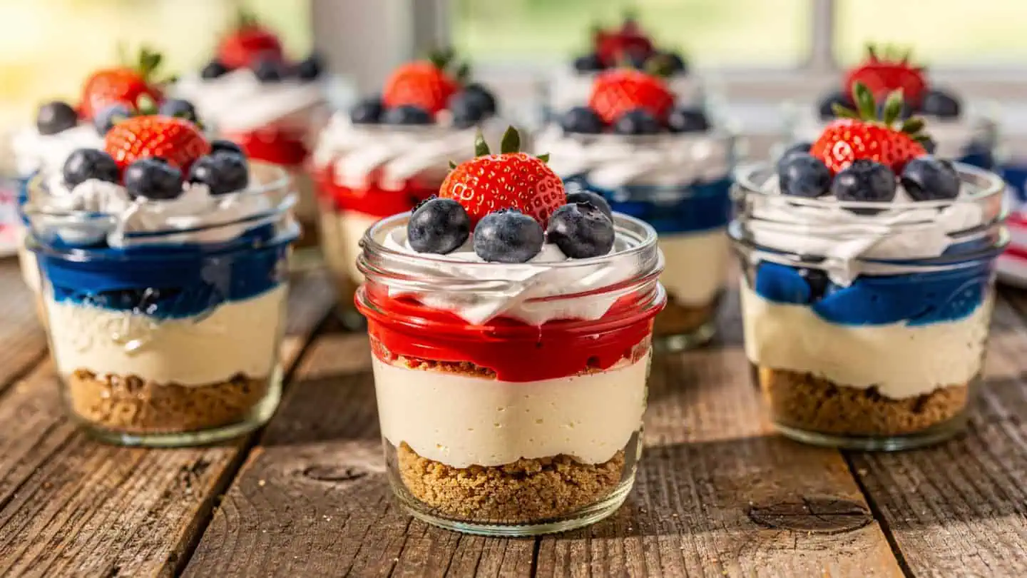 Individual no-bake cheesecake cups layered with graham cracker crust, creamy filling, strawberries, and blueberries
