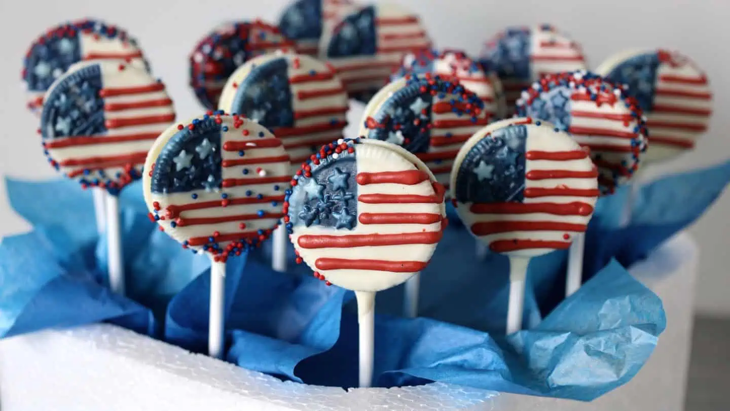 Oreo cookie pops dipped in white chocolate with red and blue sprinkles displayed for patriotic dessert table
