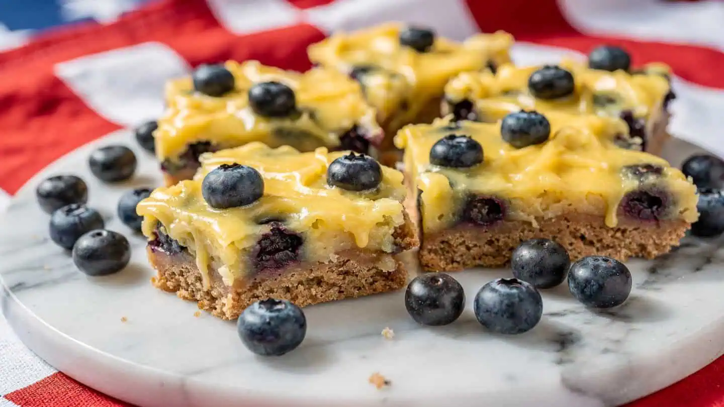 No-bake lemon blueberry dessert bars with graham cracker crust topped with fresh blueberries on marble board