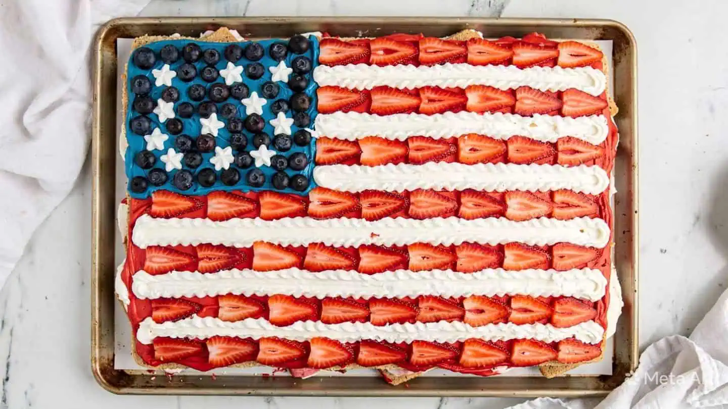 Patriotic ice cream sandwich flag cake topped with Cool Whip, strawberries, and blueberries on baking tray