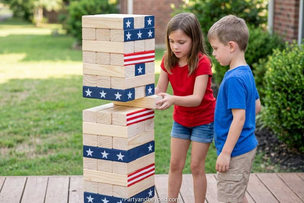 Kids playing patriotic-themed giant Jenga game outdoors.