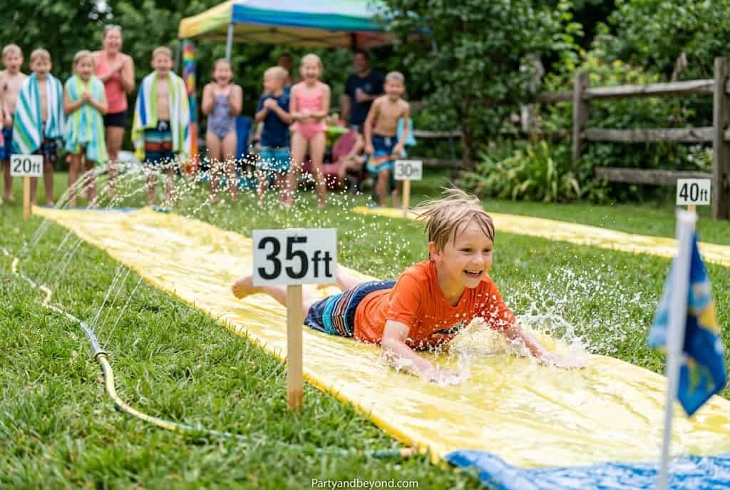 Kids enjoying a water slide at a backyard party with friends and family.