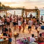 23 Brilliant Beach Party Ideas for the Most Unforgettable Summer Bash Beach party with lively crowd, DJ, and tropical decor at sunset.