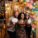12 DIY PHOTO BOOTH IDEAS FOR ANY PARTY Happy friends taking a selfie at a festive party with balloons and decorations.