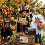 17 Halloween Scavenger Hunt Ideas (With Free Clue Examples by Age) Children in Halloween costumes enjoying pumpkin hunt and decorations.