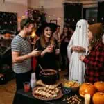 15 Last-Minute Halloween Party Ideas: Throw It Together in 3 Hours (Under $50) Group of friends in Halloween costumes enjoying spooky party with decorations and treats.