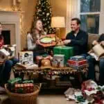 White Elephant Gift Exchange: Rules, Gift Ideas & How to Play (2026 Guide) Group of friends exchanging gifts around Christmas tree in cozy living room.