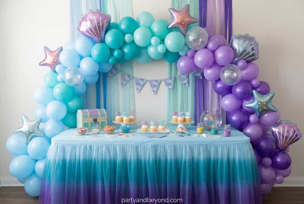 Blue, teal, and purple ombre balloon garland decorating a mermaid birthday cake table.