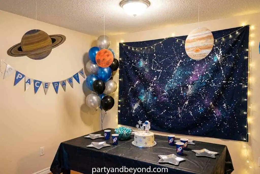 Handmade black galaxy backdrop with purple, blue, and white spray-painted stars behind a birthday cake table.