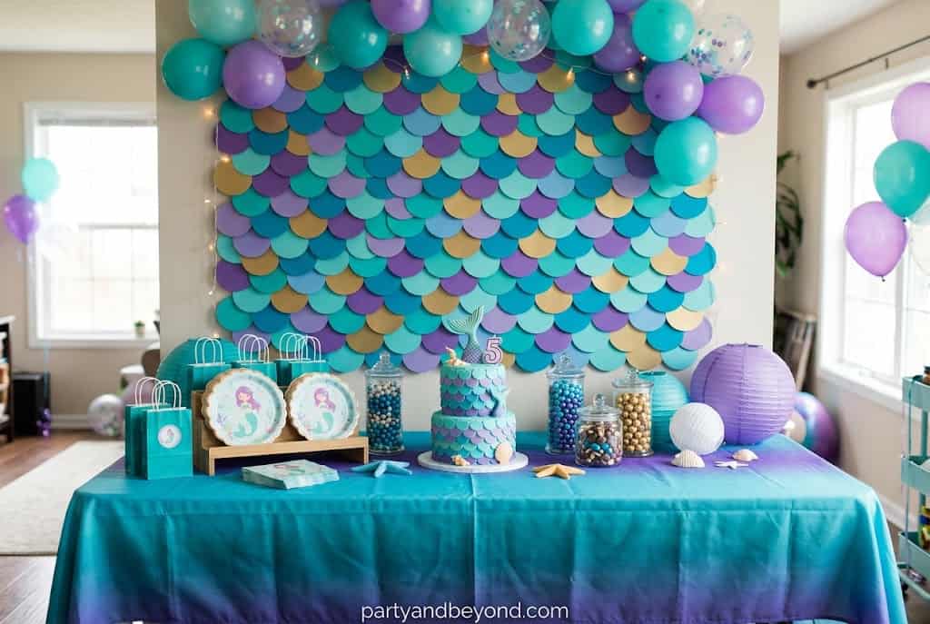 DIY mermaid scale backdrop made from overlapping colorful cardstock or paper plates.
